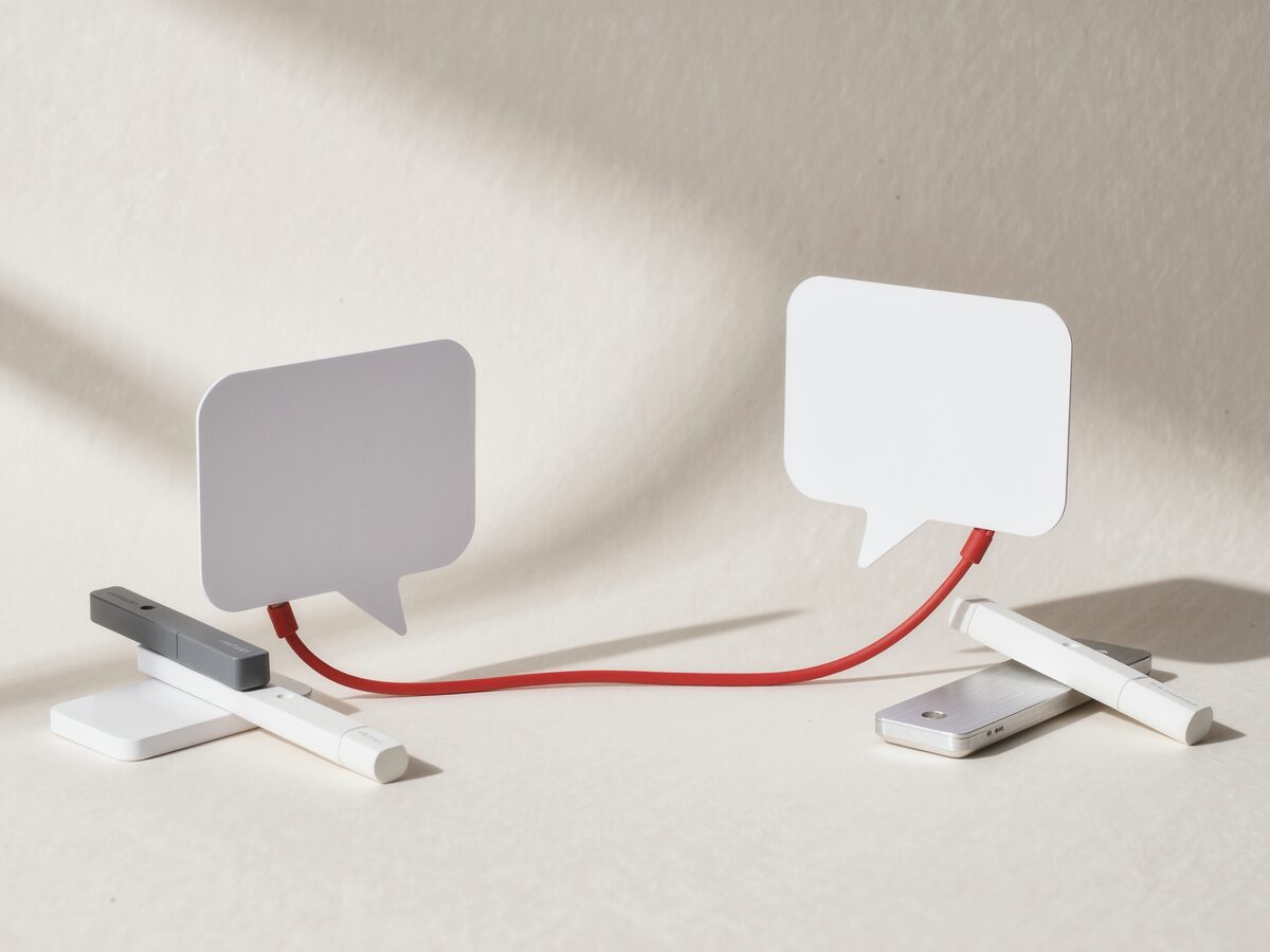 Two speech bubbles cut from thick white paper, joined by a red cable.